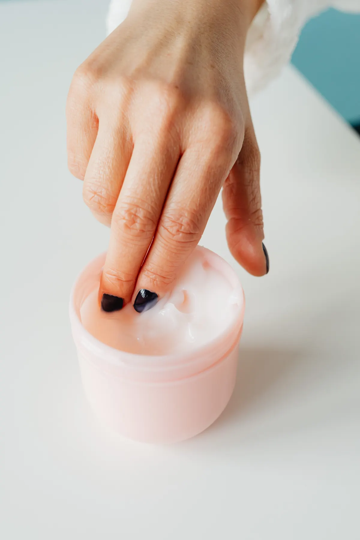 Close-up of a hand scooping Vaseline Body Oil from a jar.
